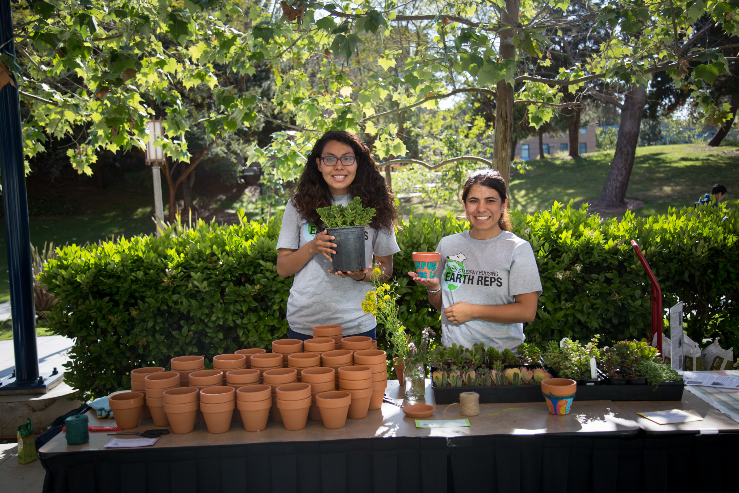 Two woman smile, holding potted plants in garden.